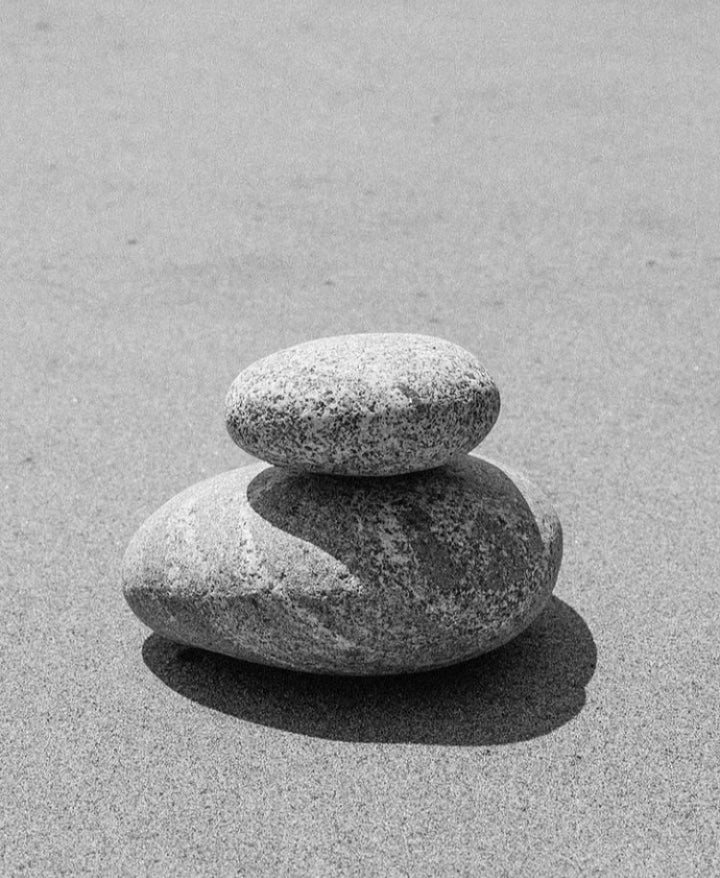 A black and white photography of a small rock balancing on top of a larger rock