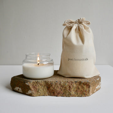 Small apothecary candle sitting next to Poet Botanicals branded cotton drawstring bag.